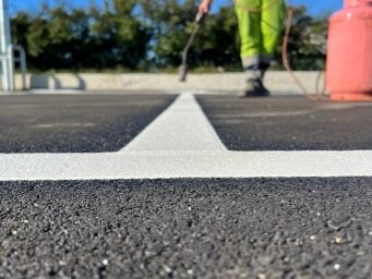 Close‑up of contractor applying Prismo preformed thermoplastic white parking bay lines with a gas torch on a car park surface in daylight.