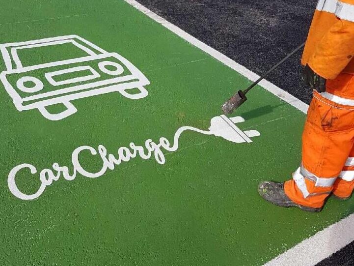 Prismo Preformed Thermoplastic white EV charging bay symbol being applied with a gas torch by a contractor in daylight. The EV bay symbol is a custom design on a refreshed green parking bay.