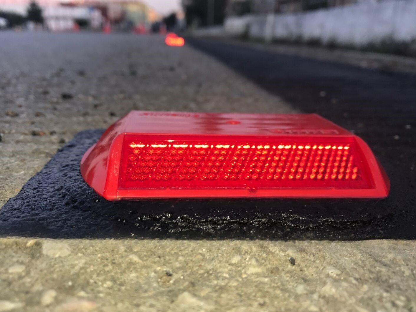 Close-up of red Stimsonite road stud bonded to road surface using Prismo Bundy Pad made from preformed thermoplastic