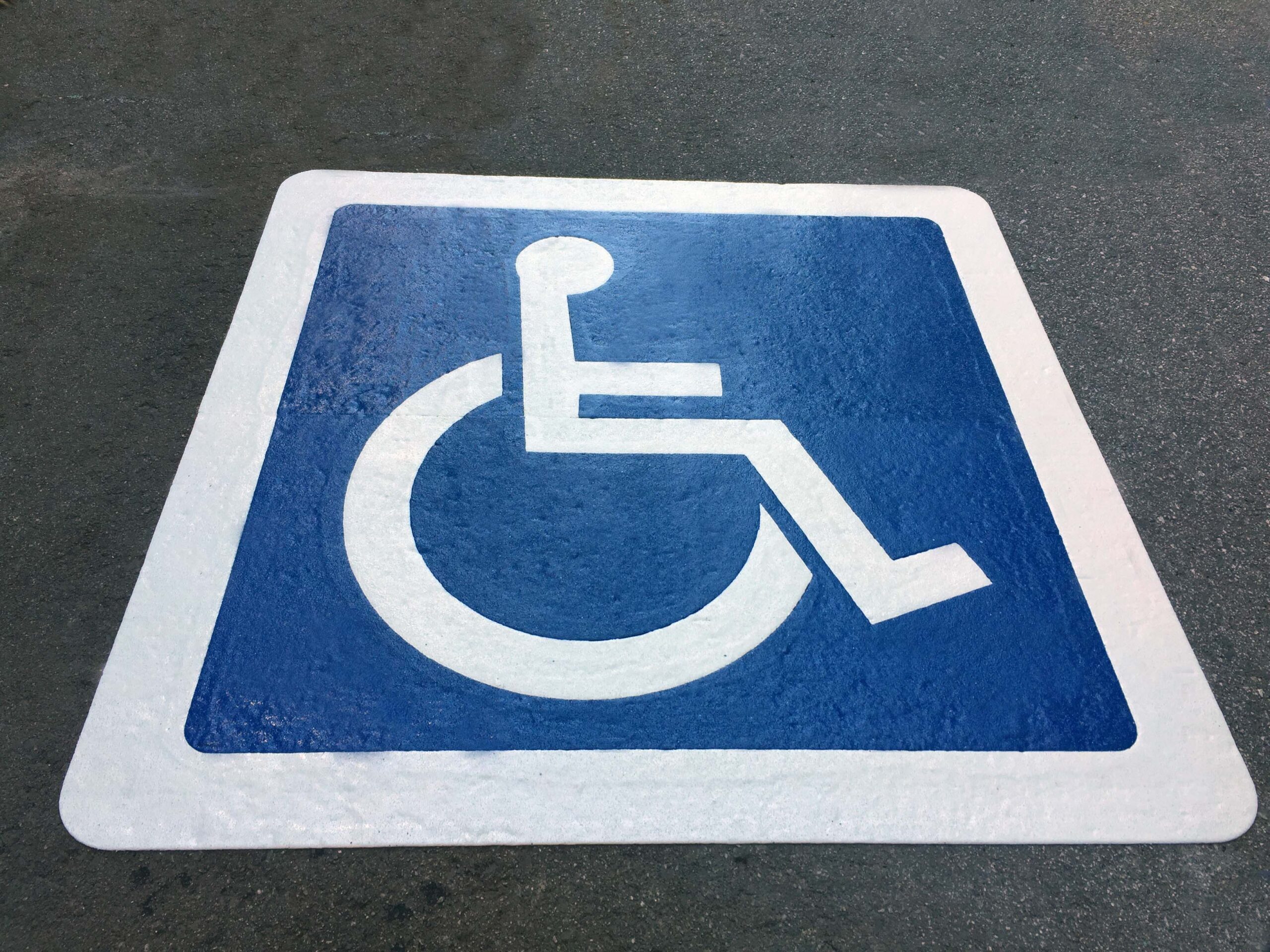 Disabled parking bay with a white wheelchair symbol on a blue background made from Prismo preformed thermoplastic symbols on asphalt surface.
