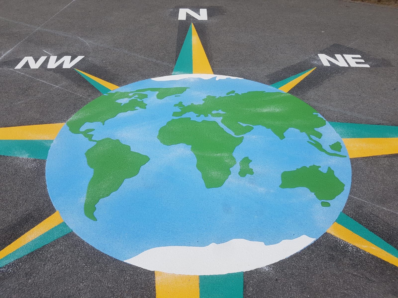Playground marking of a circular world map with compass directions made from Prismo preformed thermoplastic, showing N, S, E, W and diagonals NE, NW, SE, SW.