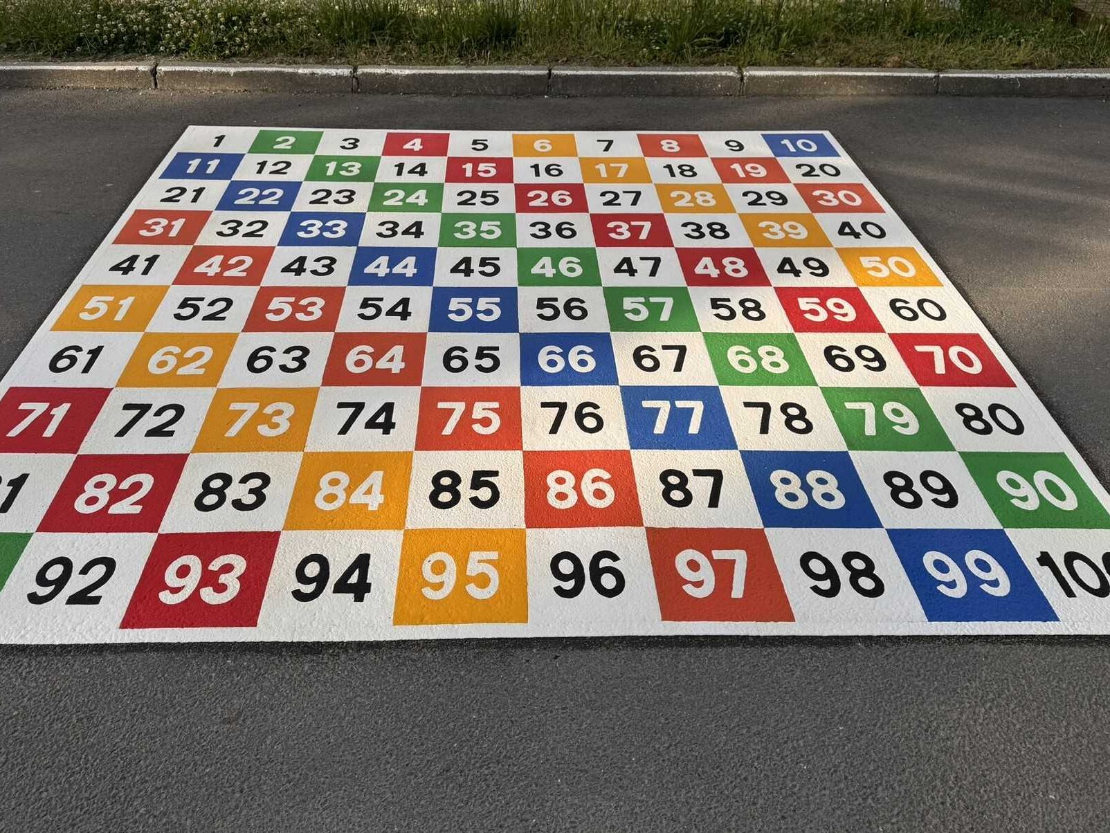 Colourful 1 to 100 number grid playground marking made from Prismo preformed thermoplastic, installed on asphalt in a playground in Germany.