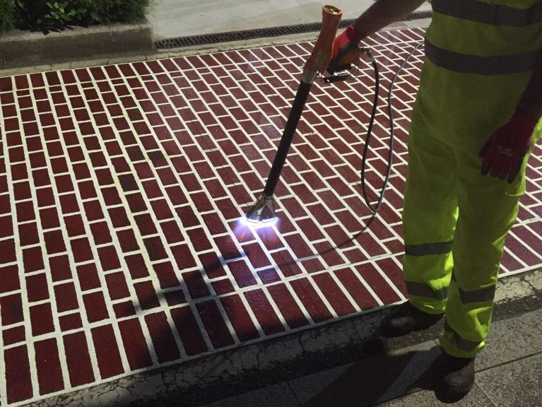 Prismo Urban Patterns preformed thermoplastic in a white and chestnut block paving design being applied to a street by a contractor using a gas torch.