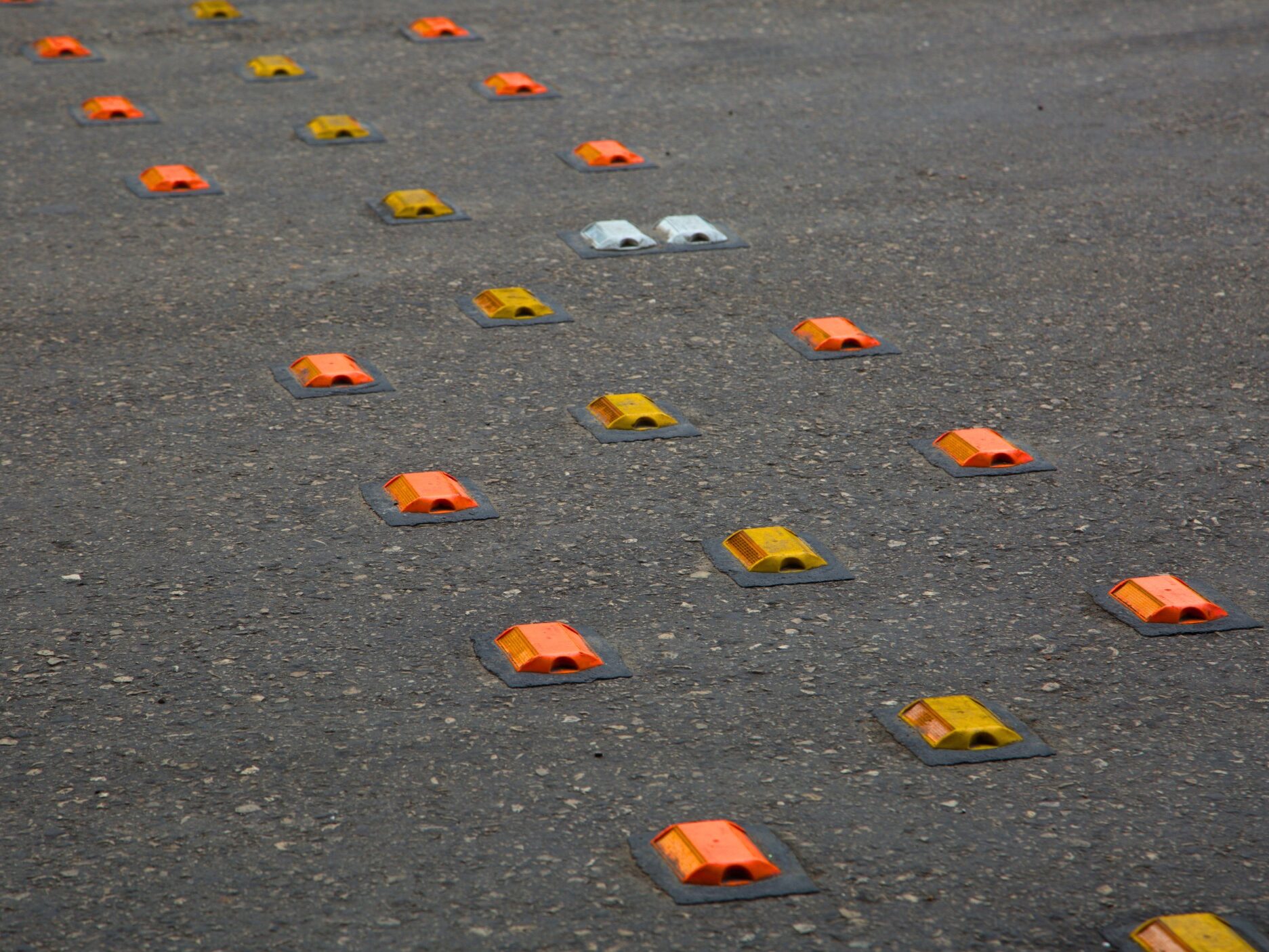 Multiple road studs in yellow, orange, and white bonded to the road surface in lines using Prismo Bundy Pads, part of the Prismo preformed thermoplastic road marking range