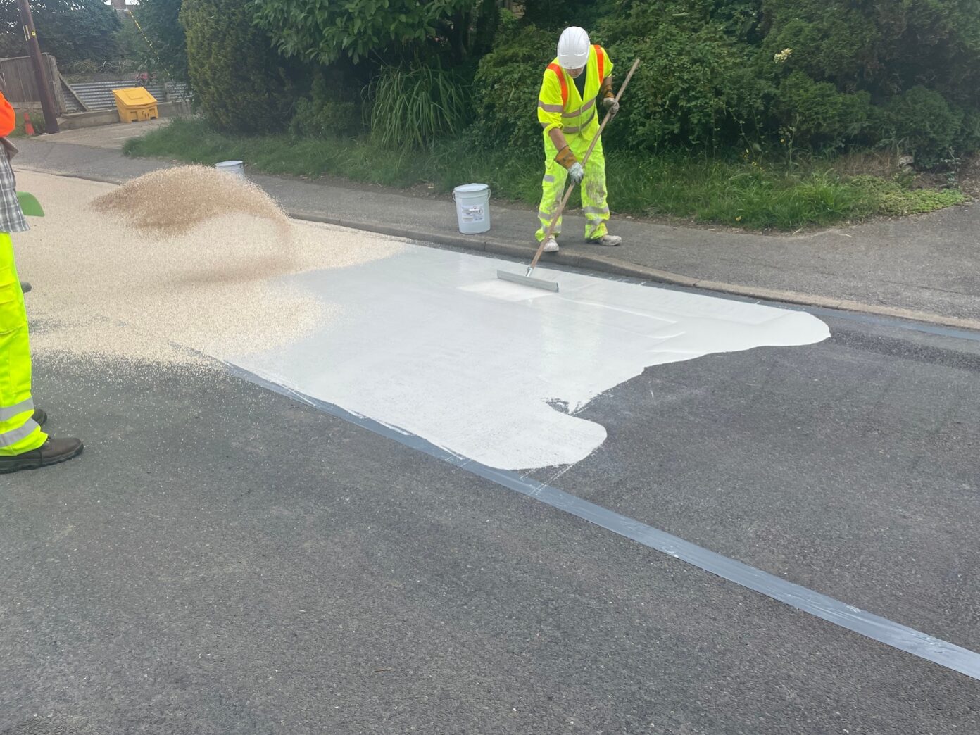 Contractors applying Prismogrip high friction surfacing using a squeegee and spreading aggregate