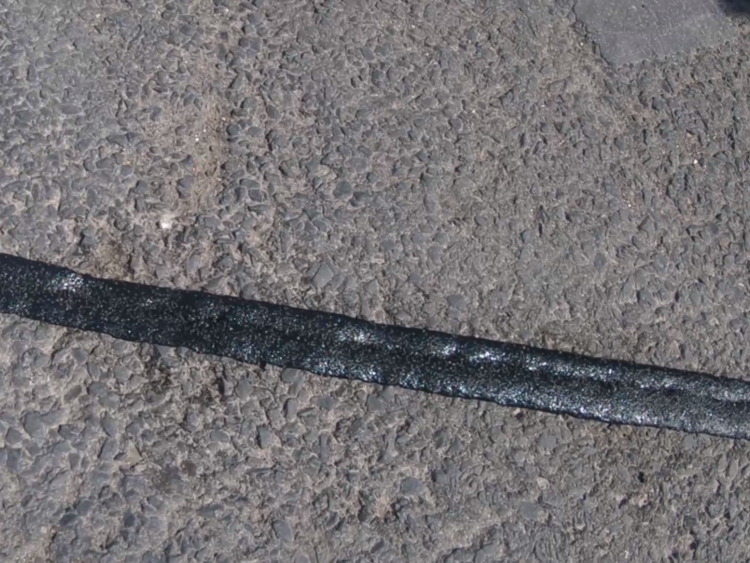 Full view of Prismo PFT Overbanding strip applied along an asphalt road surface, showing the preformed thermoplastic road marking material in place for sealing cracks and joints with visible texture and clean edges