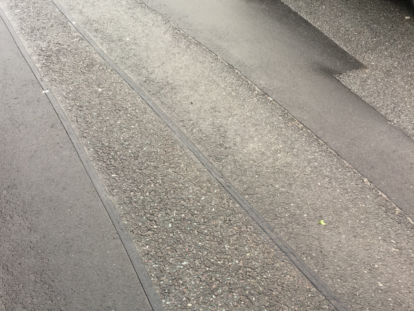 Multiple Prismo PFT Overbanding strips applied to an asphalt road surface in Oldham, showing Prismo preformed thermoplastic road marking product being effectively used to seal cracks and joints with durable, clean application lines