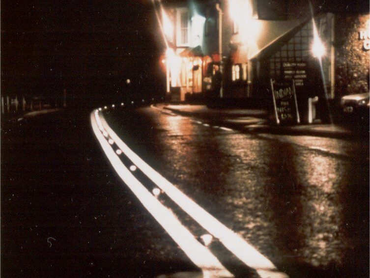 Prismo® Rainline® hot applied thermoplastic applied on a wet road surface as a white profiled line marking following the bend of the road at night.