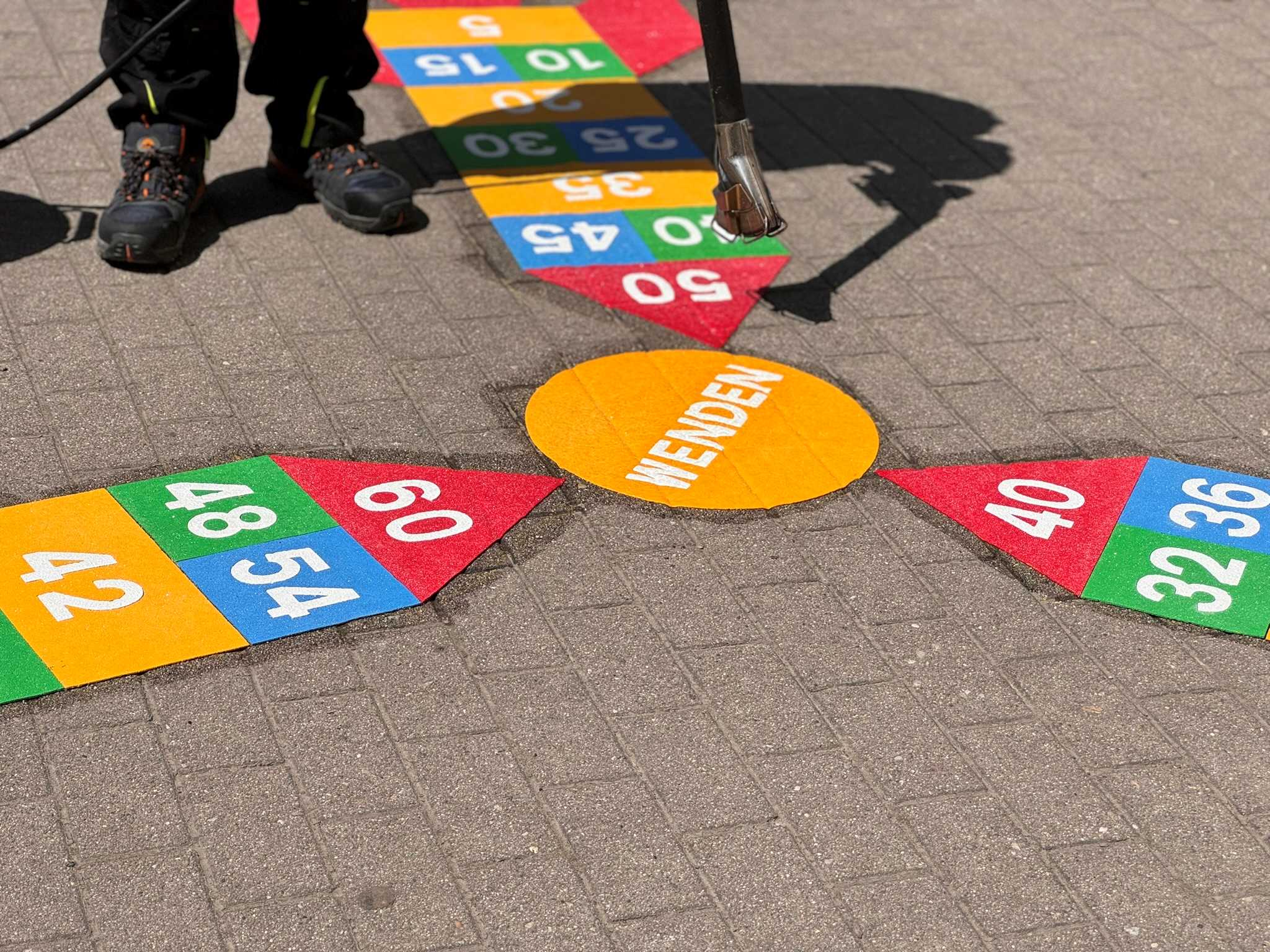 Contractor applying a colourful rocket ship times table design to a playground in Germany using a gas torch and Prismo preformed thermoplastic road markings.