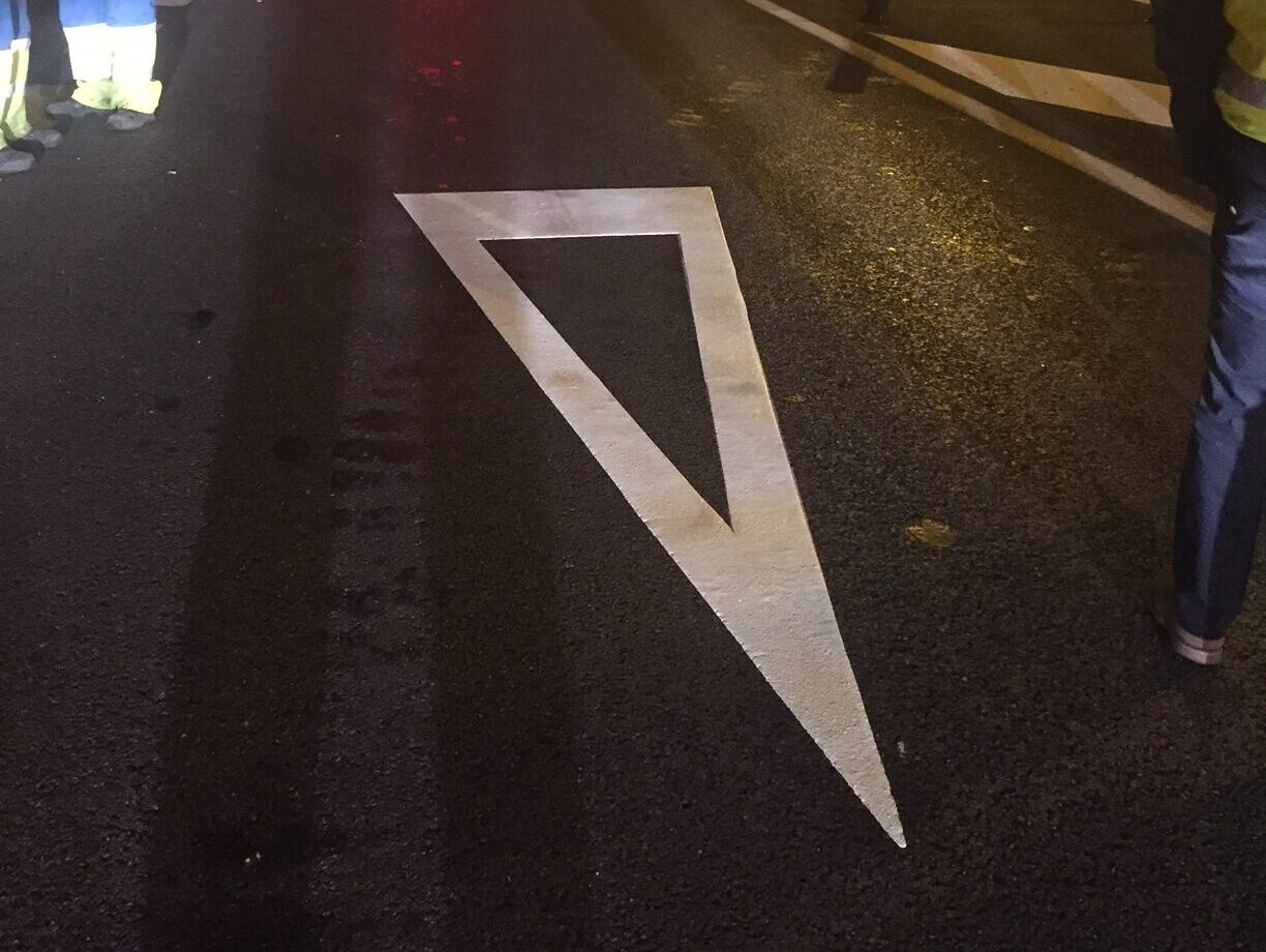 This image shows a white preformed thermoplastic give way marking applied to a motorway in Spain, at night time.