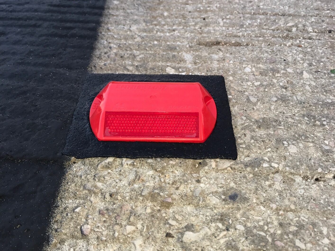 Side view of a single red Stimsonite road stud bonded to a concrete road surface using a Prismo Bundy Pad made from Prismo preformed thermoplastic