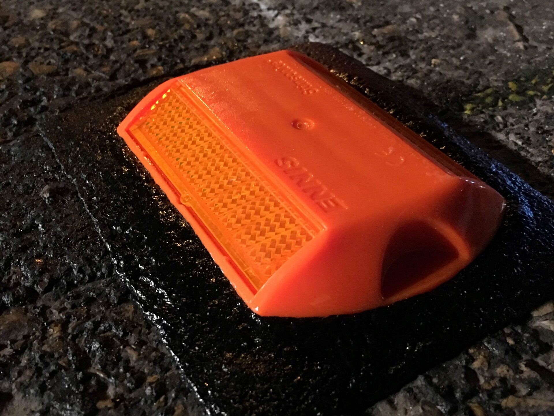 Close-up of an orange road stud bonded to the road surface using a Prismo Bundy Pad made from Prismo preformed thermoplastic