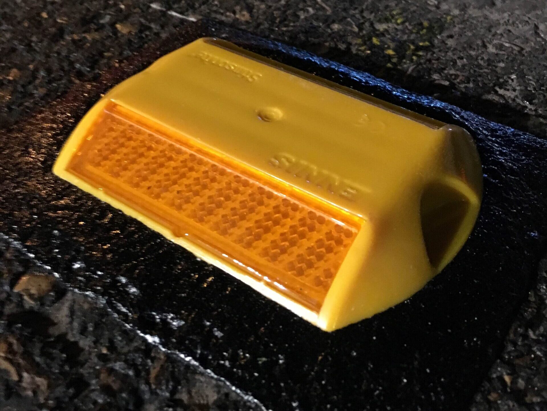 Close-up of a yellow road stud bonded to the road surface using a Prismo Bundy Pad made from Prismo preformed thermoplastic