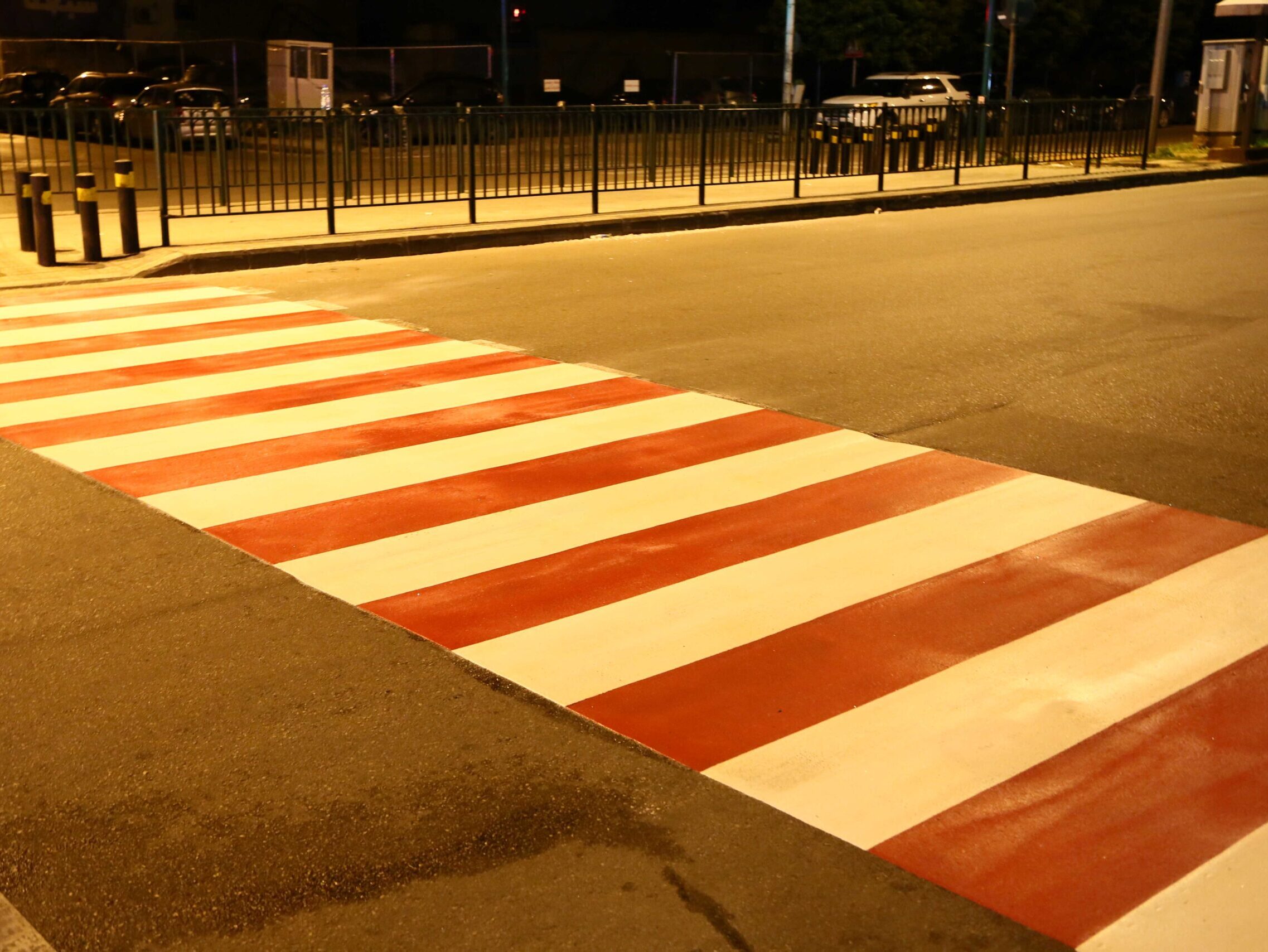 This Image shows a white and red preformed thermoplastic pedestrian crossing at night time on a street lit road.