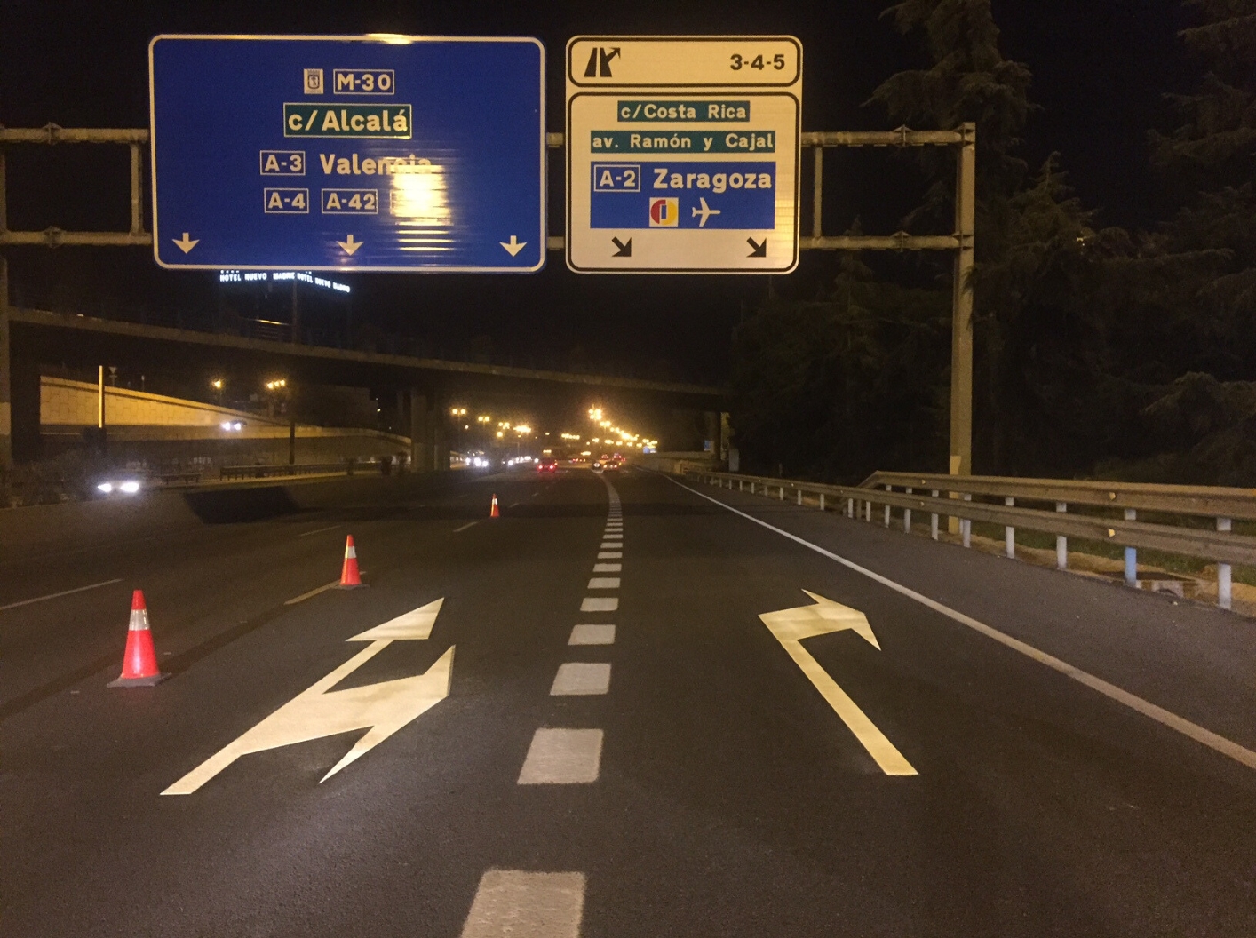 Two Prismo® Preformed thermoplastic white arrows on a motorway in Spain at night. Above the arrow markings is two motorway signs giving additional directions.