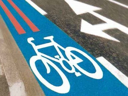 Blue Prismo Cycletrack high-friction surfacing marking a dedicated cycle lane at a busy road junction, featuring a white bicycle symbol to clearly indicate the lane is for cyclists