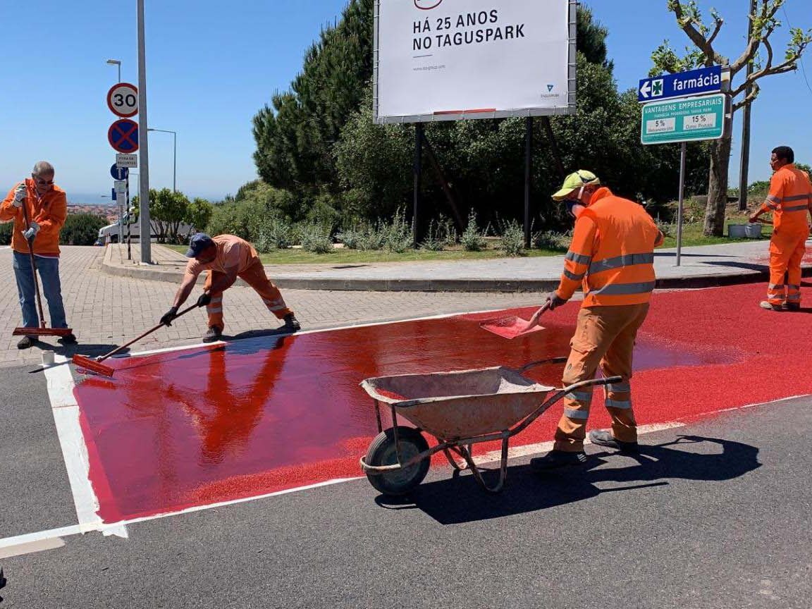 Contractors applying red Prismo Tyregrip high friction surfacing product with squeegees and spreading aggregate in Portugal on a sunny day